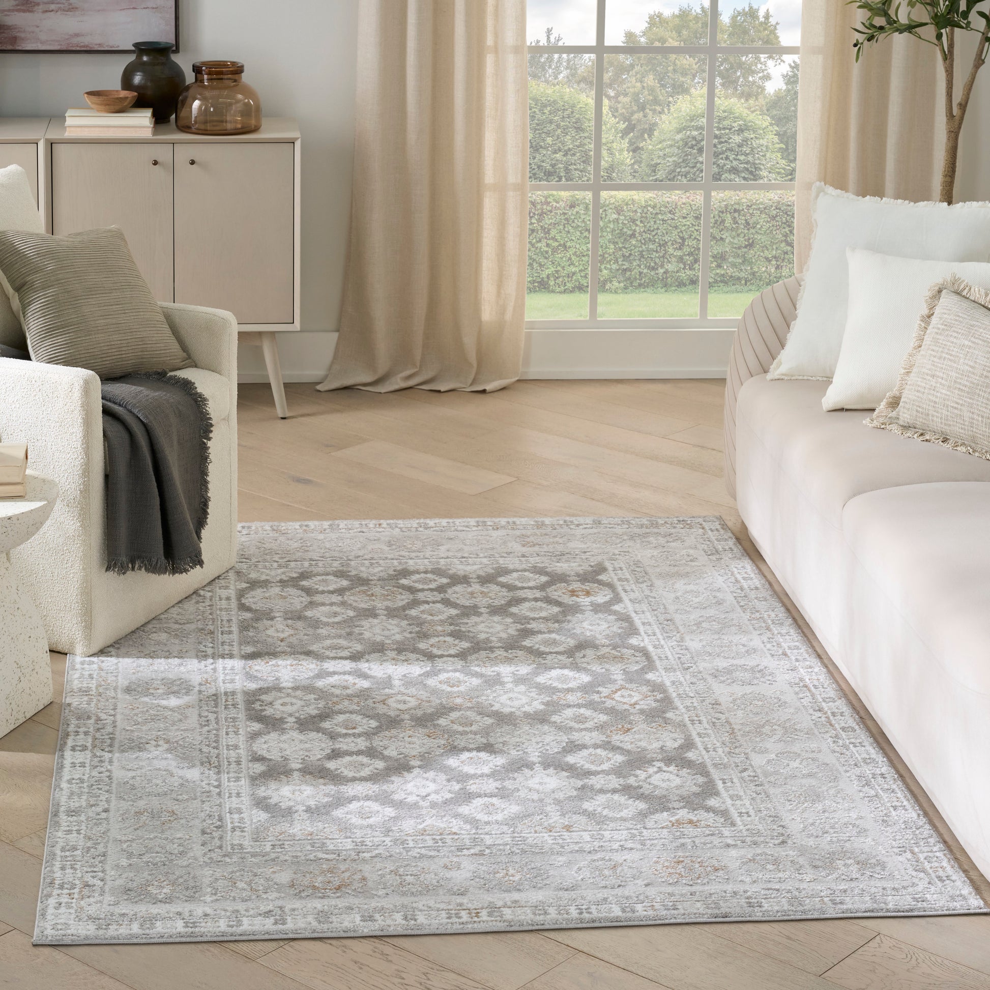 Light grey and ivory patterned area rug with a distressed motif on a pale wood floor in a neutral living room.