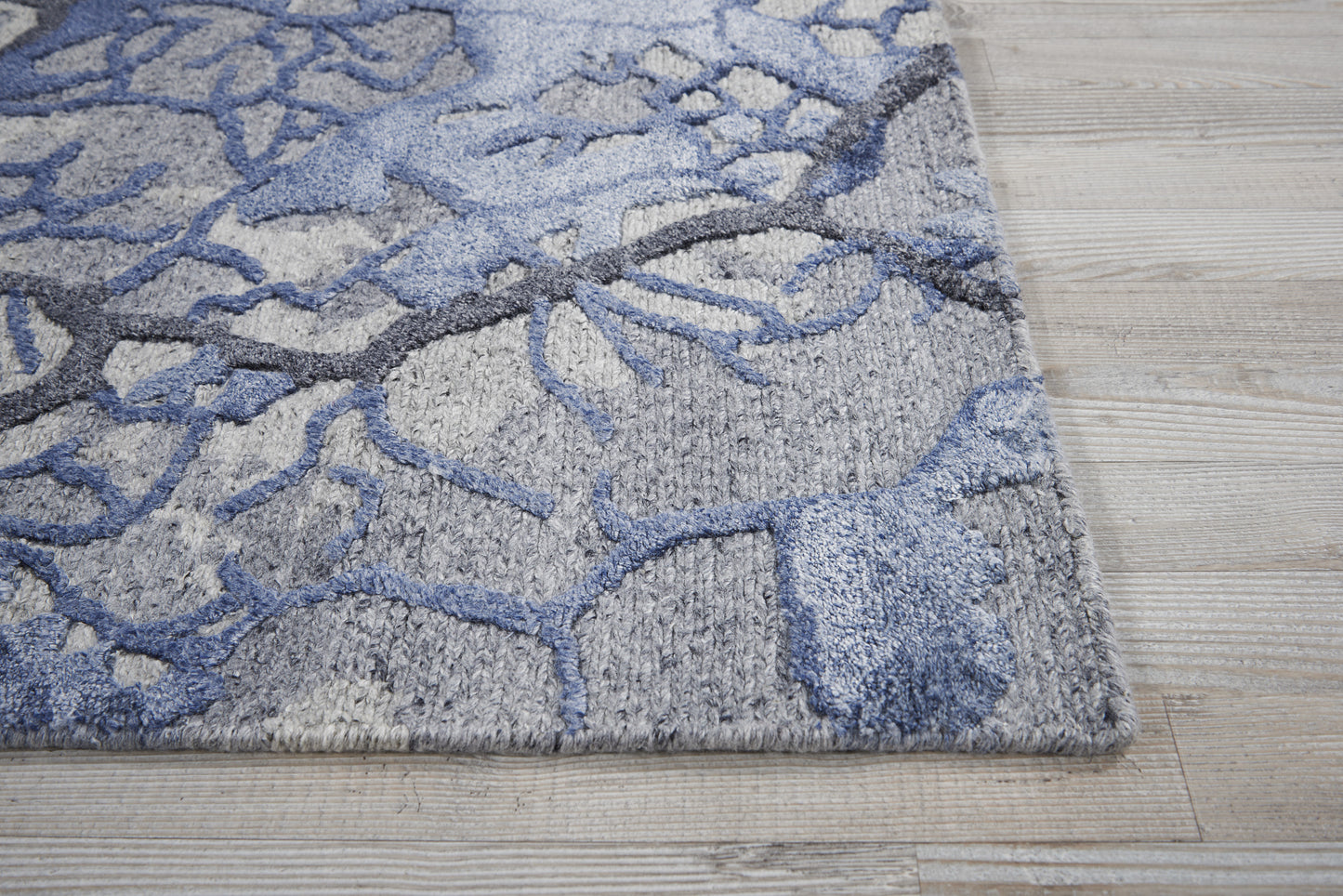 Gray area rug with blue abstract branching pattern and plush textured pile on a light wood floor.