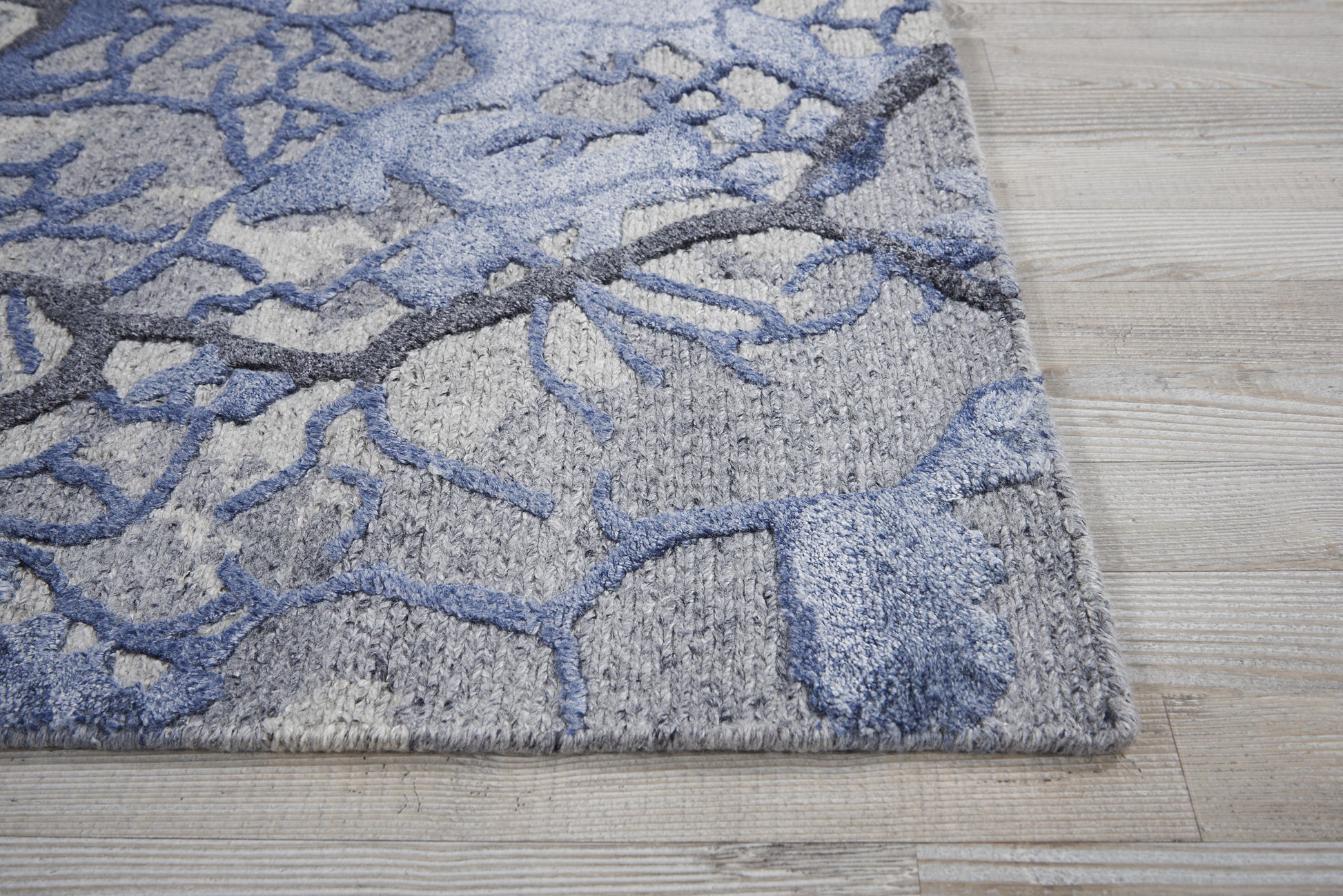 Gray area rug with blue abstract branching pattern and plush textured pile on a light wood floor.