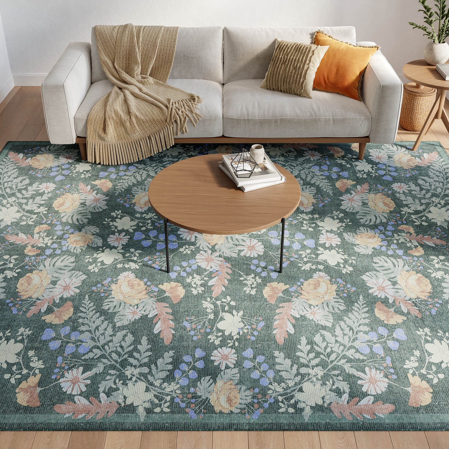 Living room scene with a round wood coffee table on a blue floral rug, beige sofa with mustard and orange cushions and a beige throw.