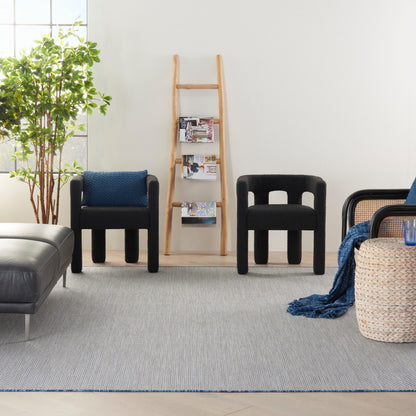 Modern living room with black armless chairs, a wooden ladder shelf, tall plant, grey rug, and a woven basket with blue throw.