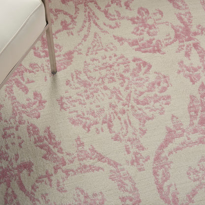 Beige rug with pink damask floral pattern; corner of light sofa with metal leg visible.