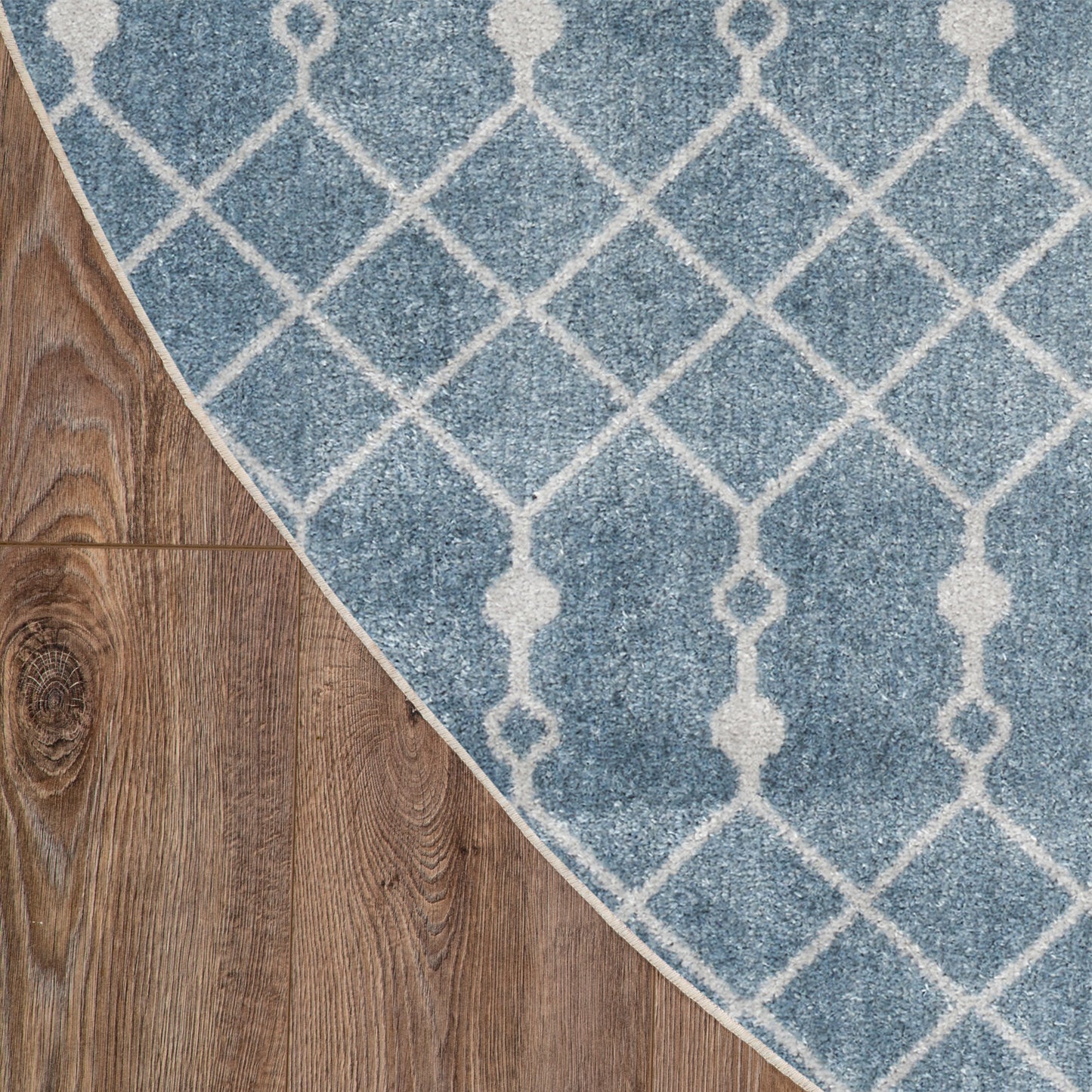 Blue rug with white geometric lattice pattern on wood floor; curved edge reveals brown planks.