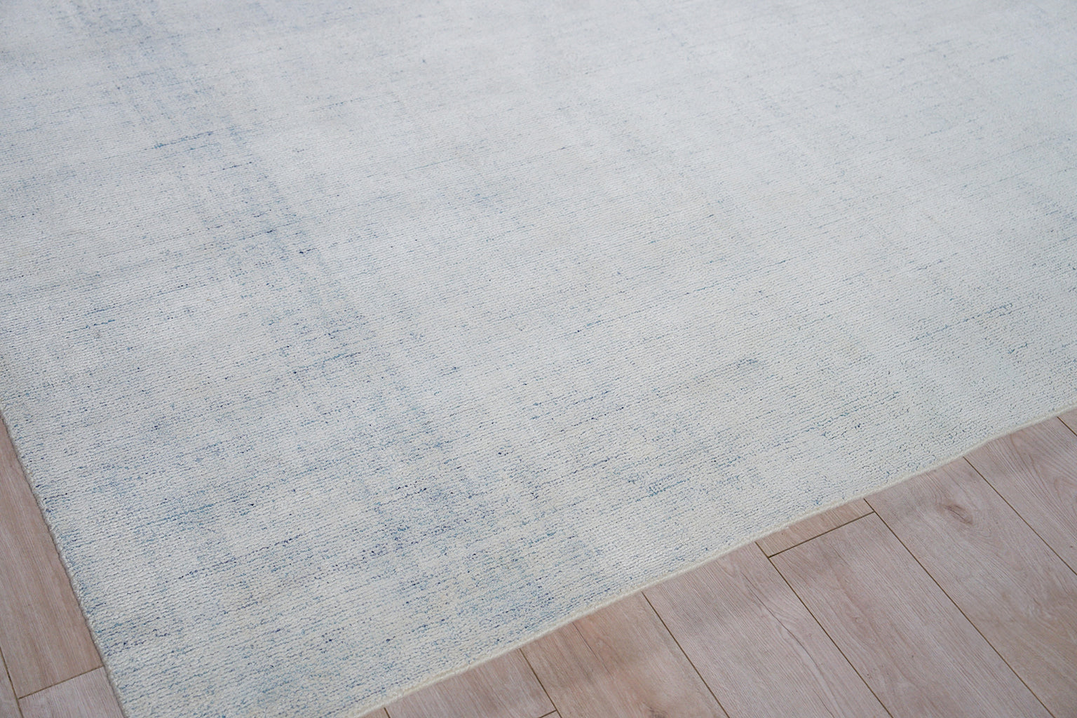 Light blue flat-weave area rug with subtle distressed texture on wood floor.