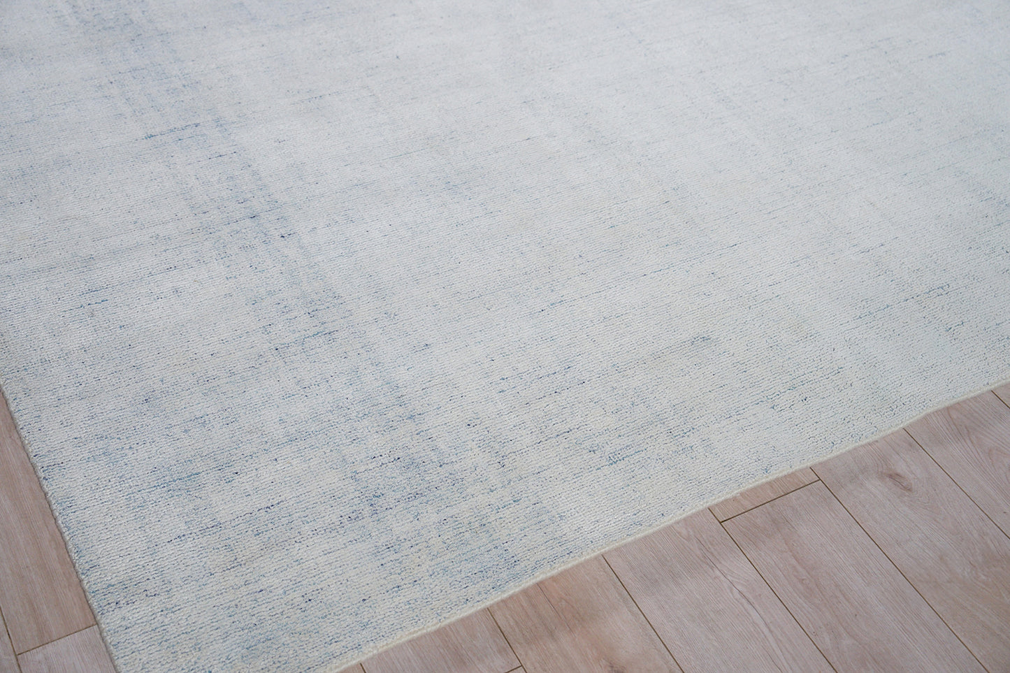 Rectangular light blue area rug with a subtle mottled texture on pale wood flooring.