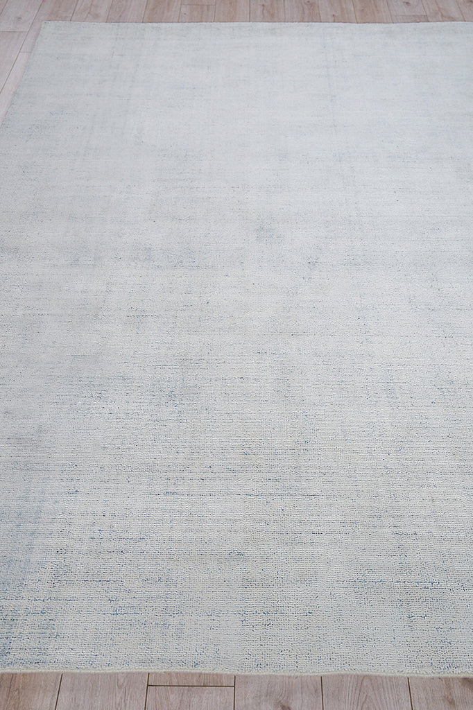 Light blue-gray rectangular rug with subtle woven texture laid on a wooden floor.