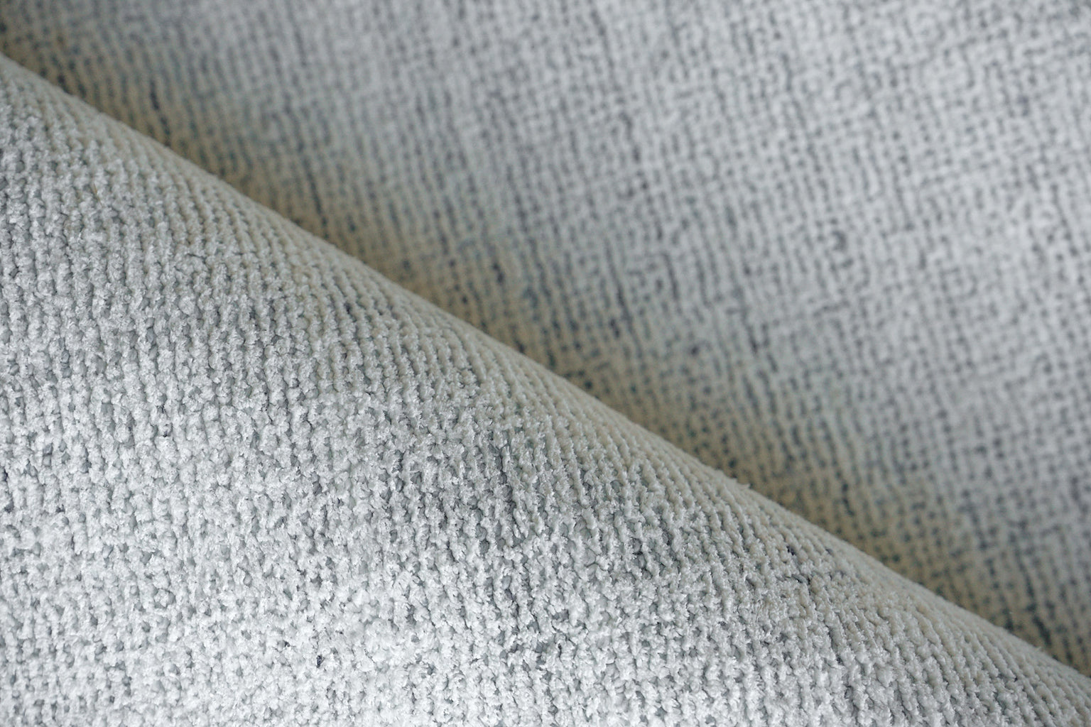 Close-up of a light gray boucle rug with textured looped pile and a soft draped fold.
