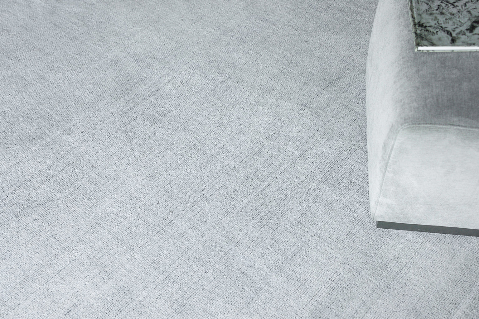 Light gray textured rug in a modern living room with a light-gray upholstered sofa nearby; hand-loomed 8' x 10' rug.