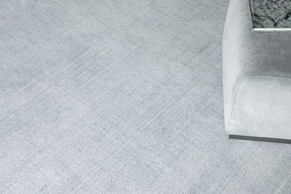 Light gray textured rug in a modern living room with a light-gray upholstered sofa nearby; hand-loomed 8' x 10' rug.
