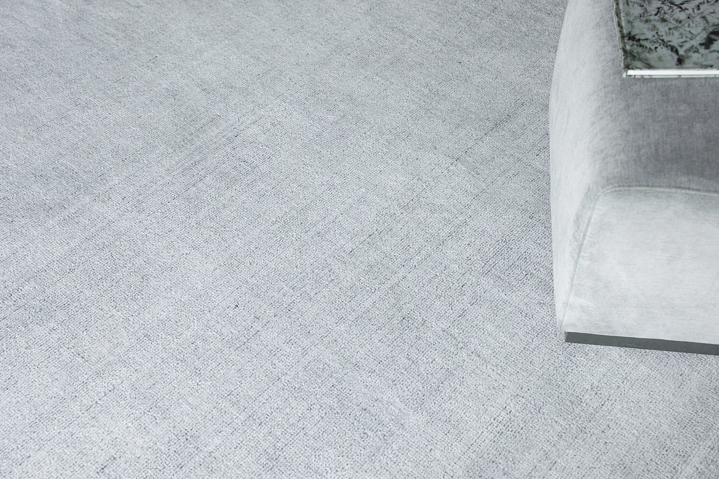 Soft light-gray textured rug with a corner view of a light gray upholstered sofa.
