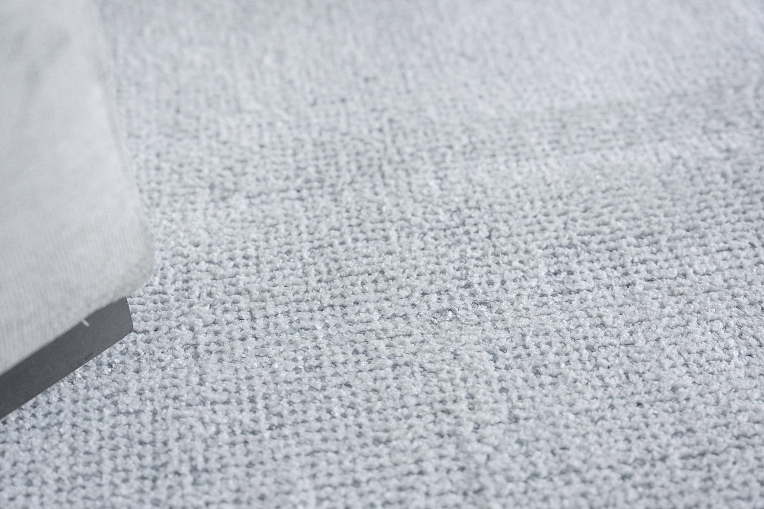 Close-up of light gray loop-pile rug with a gray fabric sofa leg at the edge