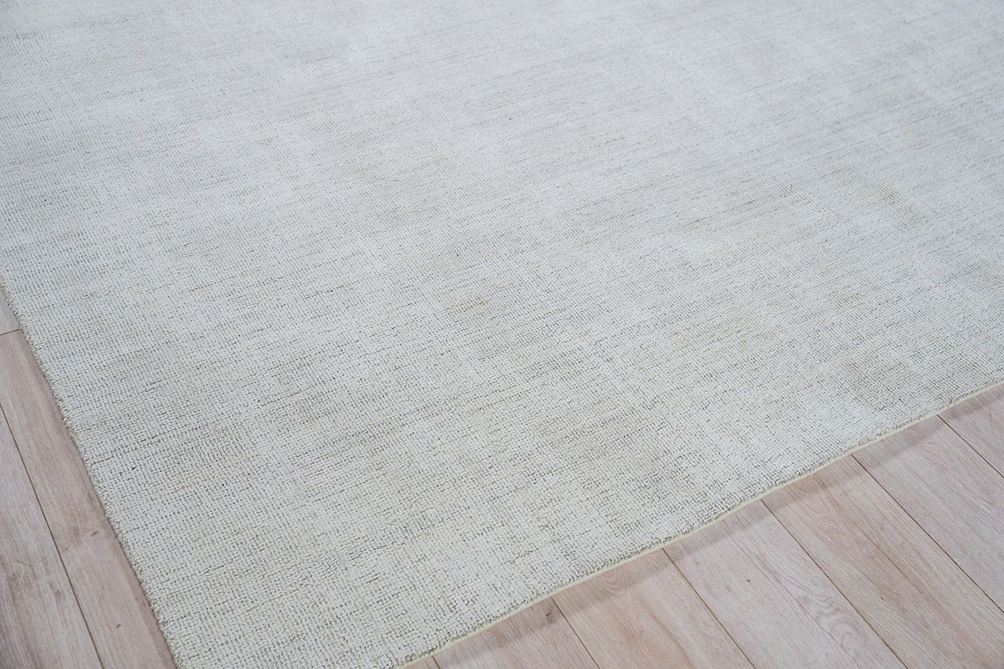 Cream-beige hand loomed rug with subtle textured weave on light wood floor.