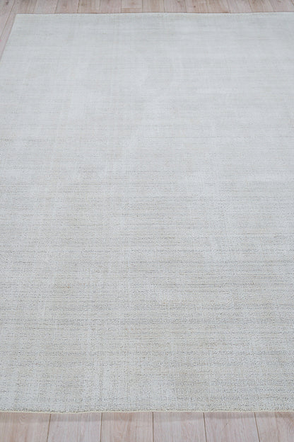 Rectangular light cream flatweave rug with subtle texture on light wood floor.