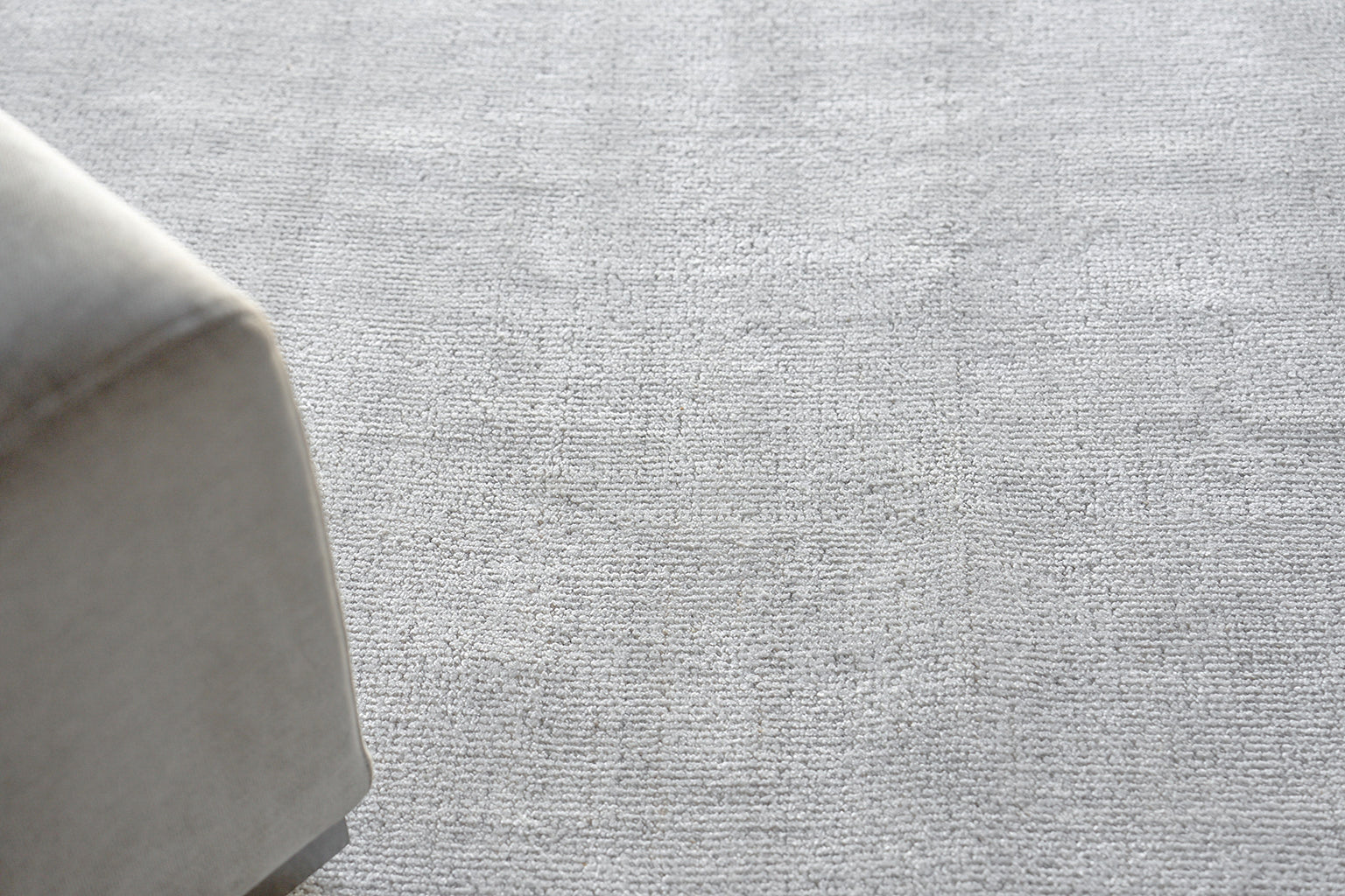 Light gray hand-loomed rug on the floor with a textured gray backdrop.