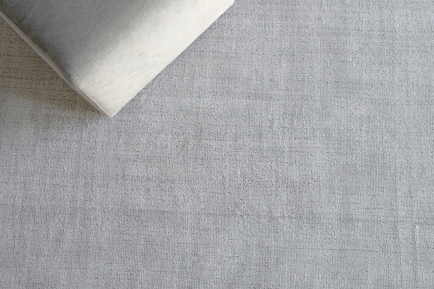 Gray textured rug with subtle woven pattern and a pale cushion resting on its top-left corner.
