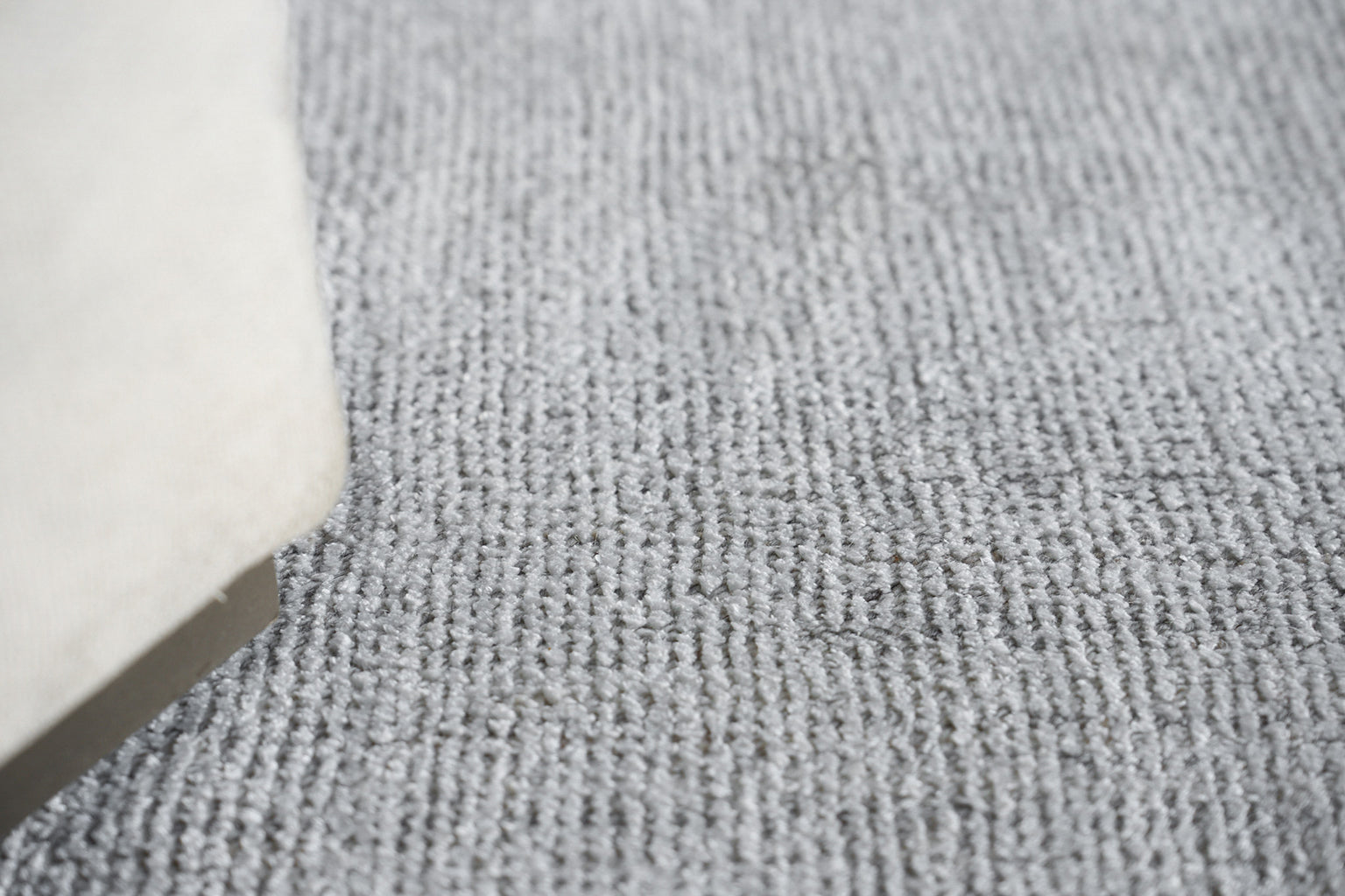 Close-up of gray textured loop-pile rug; partial white furniture edge visible in lower left.