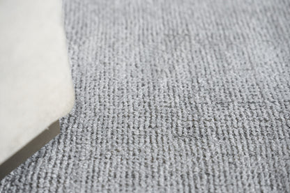 Light gray textured loop-pile rug with a beige sofa leg along the left edge.