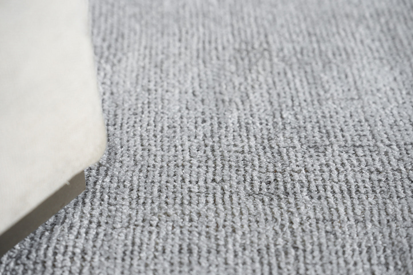 Grey textured loop-pile rug with a beige furniture leg peeking in, contemporary living room style.