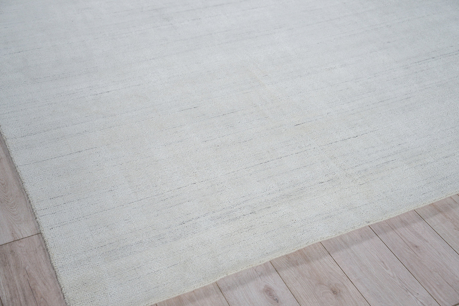 Rectangular light gray-beige rug with subtle woven texture on pale wood flooring.