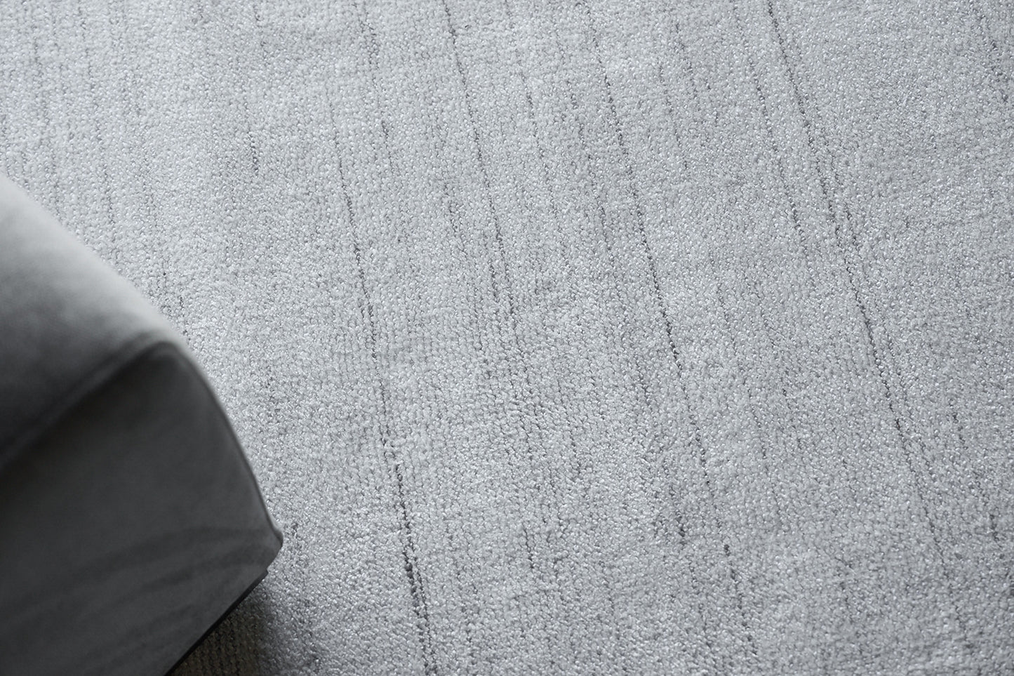 Gray textured rug with vertical stripe pattern; corner of a dark gray sofa visible.