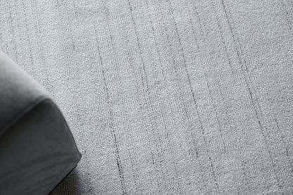 Gray textured rug with vertical stripe pattern; corner of a dark gray sofa visible.