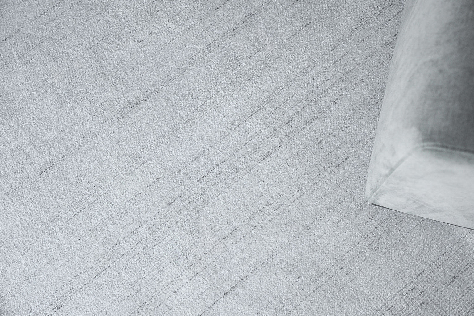 Light gray textured rug with faint diagonal lines; corner of a gray upholstered sofa visible.