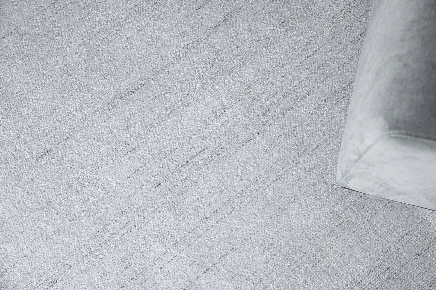 Light gray textured rug with a corner of a soft gray fabric sofa.