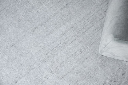 Light gray textured rug with a corner of a soft gray fabric sofa.