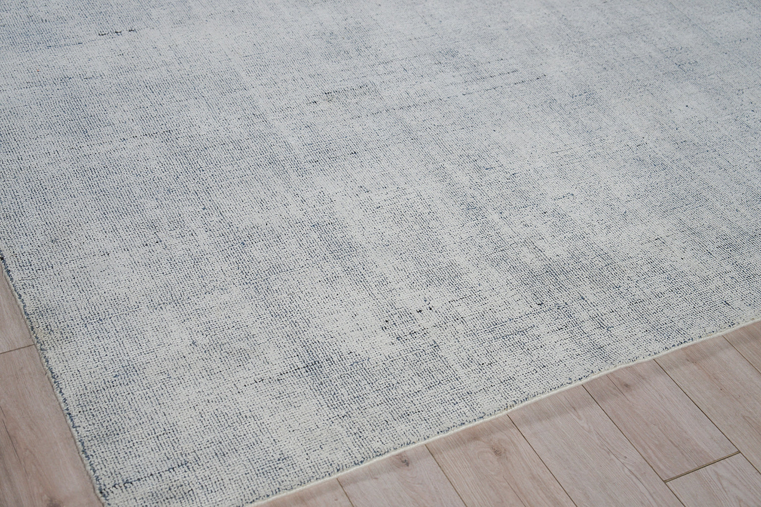 Light grey-blue woven rug with subtle texture on light wood flooring.