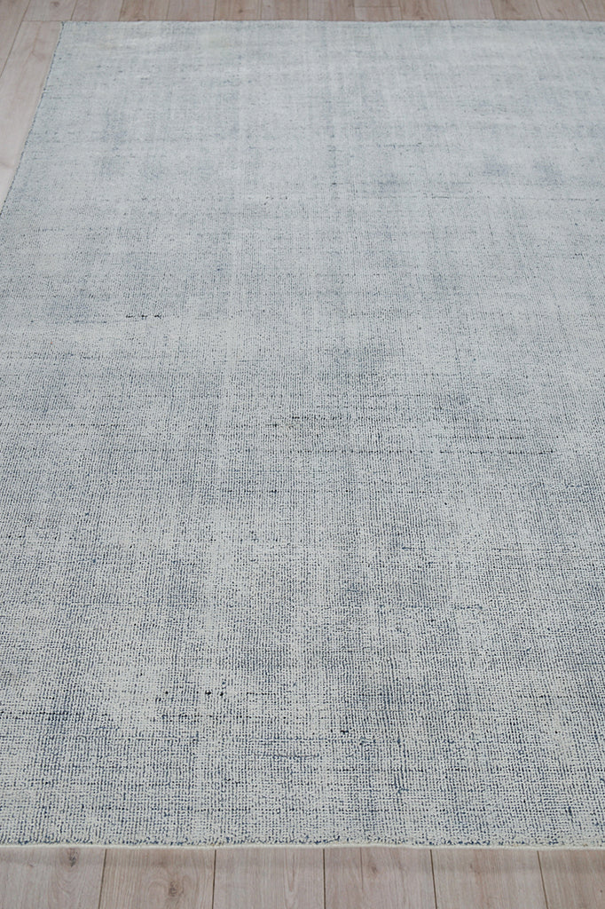 Rectangular light gray-blue hand-loomed rug with a subtle distressed texture on a wood floor.