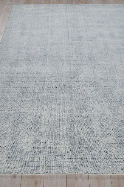Rectangular light gray-blue hand-loomed rug with a subtle distressed texture on a wood floor.