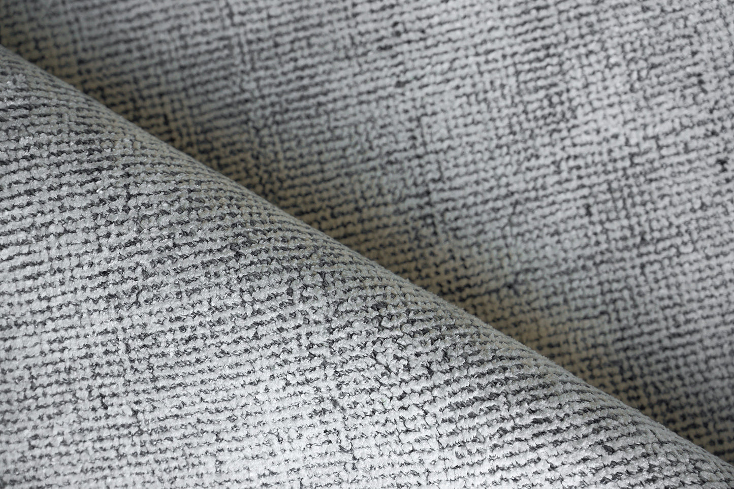 Grey textured woven rug with a heathered tweed pattern, folded to show its texture.