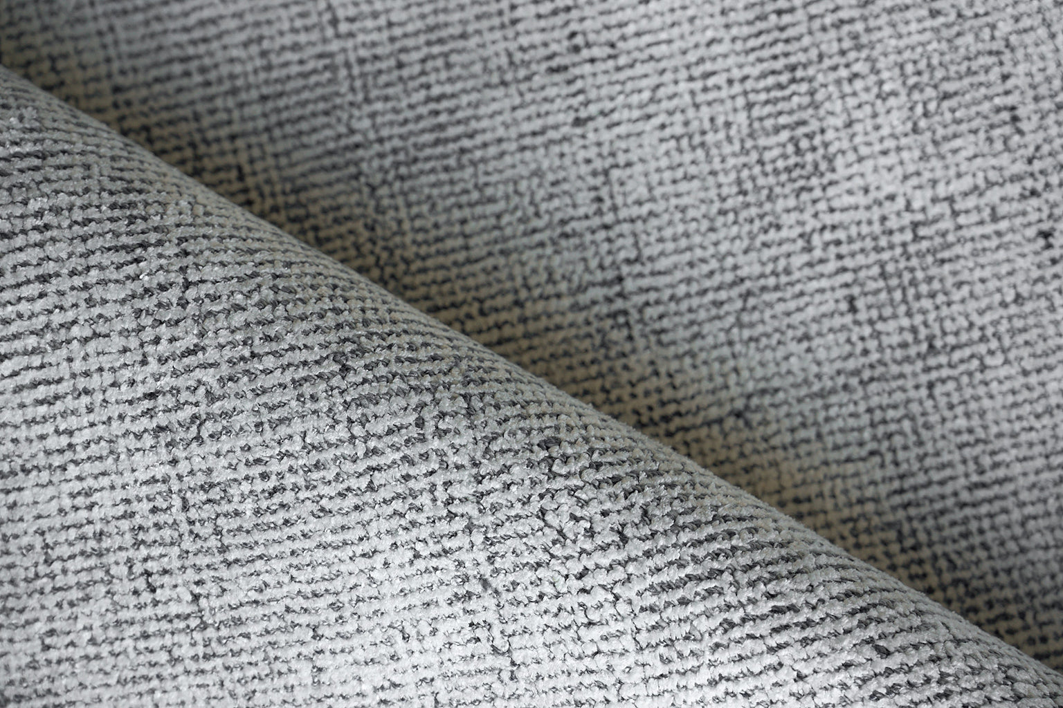 Grey textured woven rug with a heathered tweed pattern, folded to show its texture.