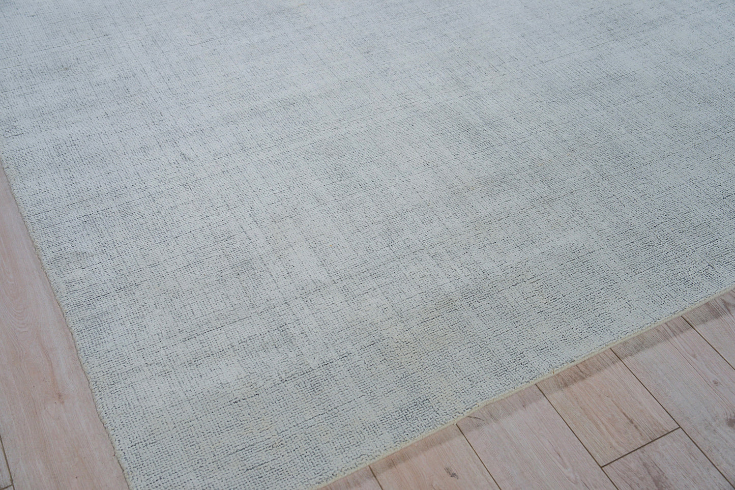 Light blue-gray hand loomed rug with subtle textured pattern on pale wood floor.