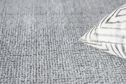 Gray textured rug with a corner of a white pillow featuring black geometric lines.