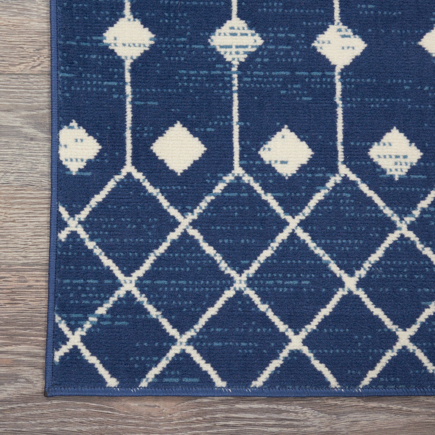 Blue area rug with white geometric lattice and diamond motifs on a wood floor.