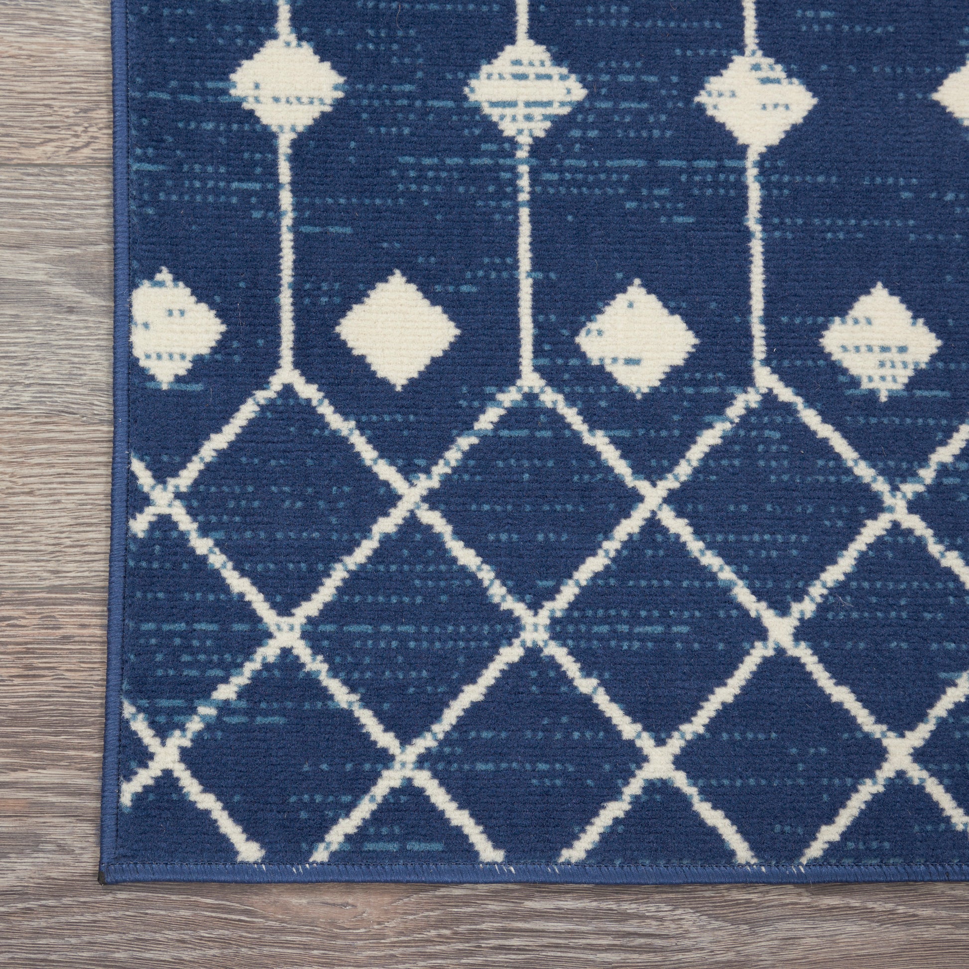 Blue area rug with white geometric lattice and diamond motifs on a wood floor.
