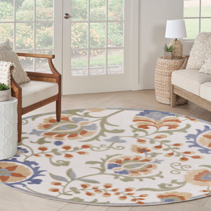 Round floral-pattern outdoor rug in ivory with orange, blue, green and taupe swirls; outdoor space with wicker accents.