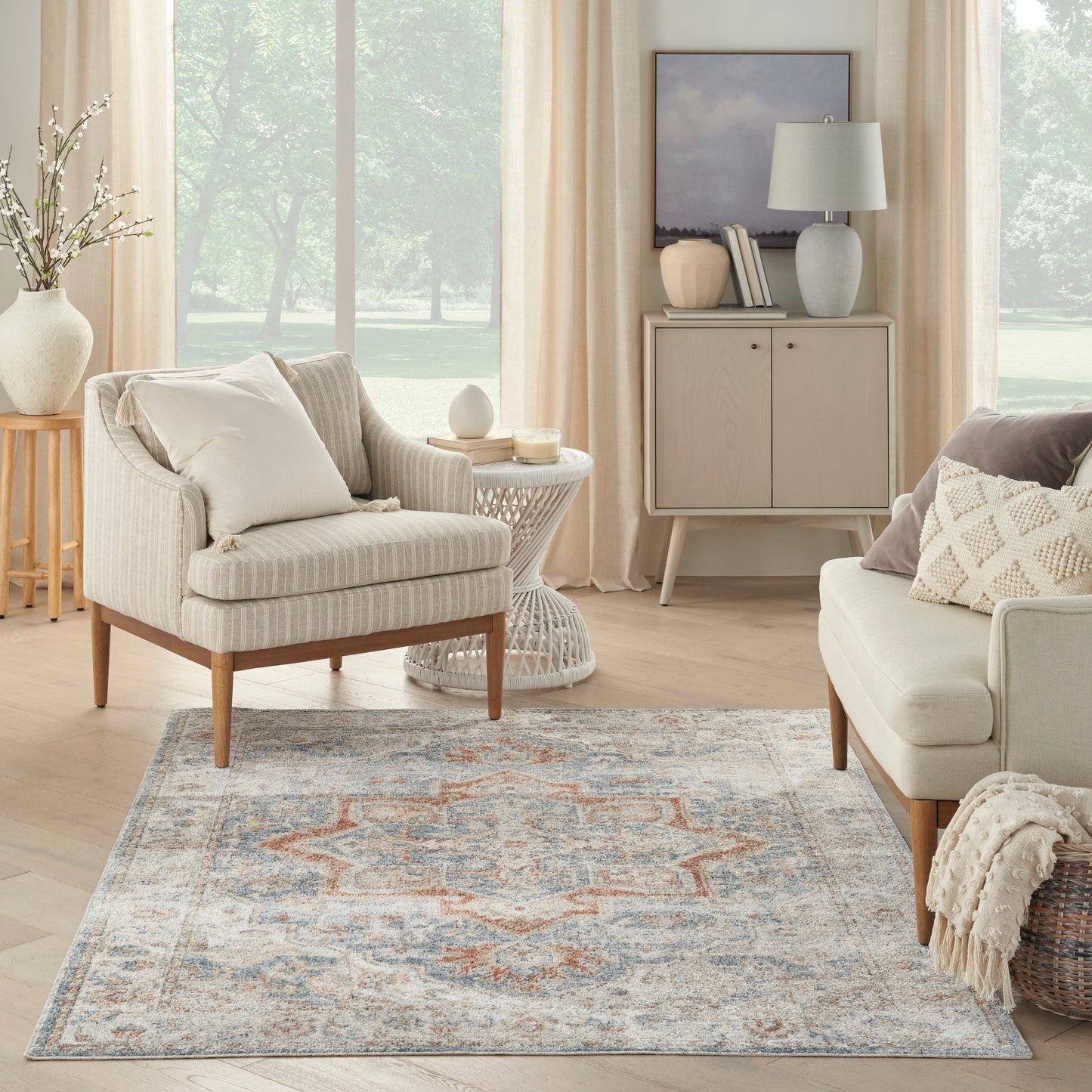 Blue-gray geometric area rug with orange accents in a neutral living room on light wood floors.