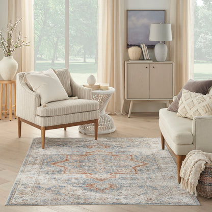 Blue-gray geometric area rug with orange accents in a neutral living room on light wood floors.
