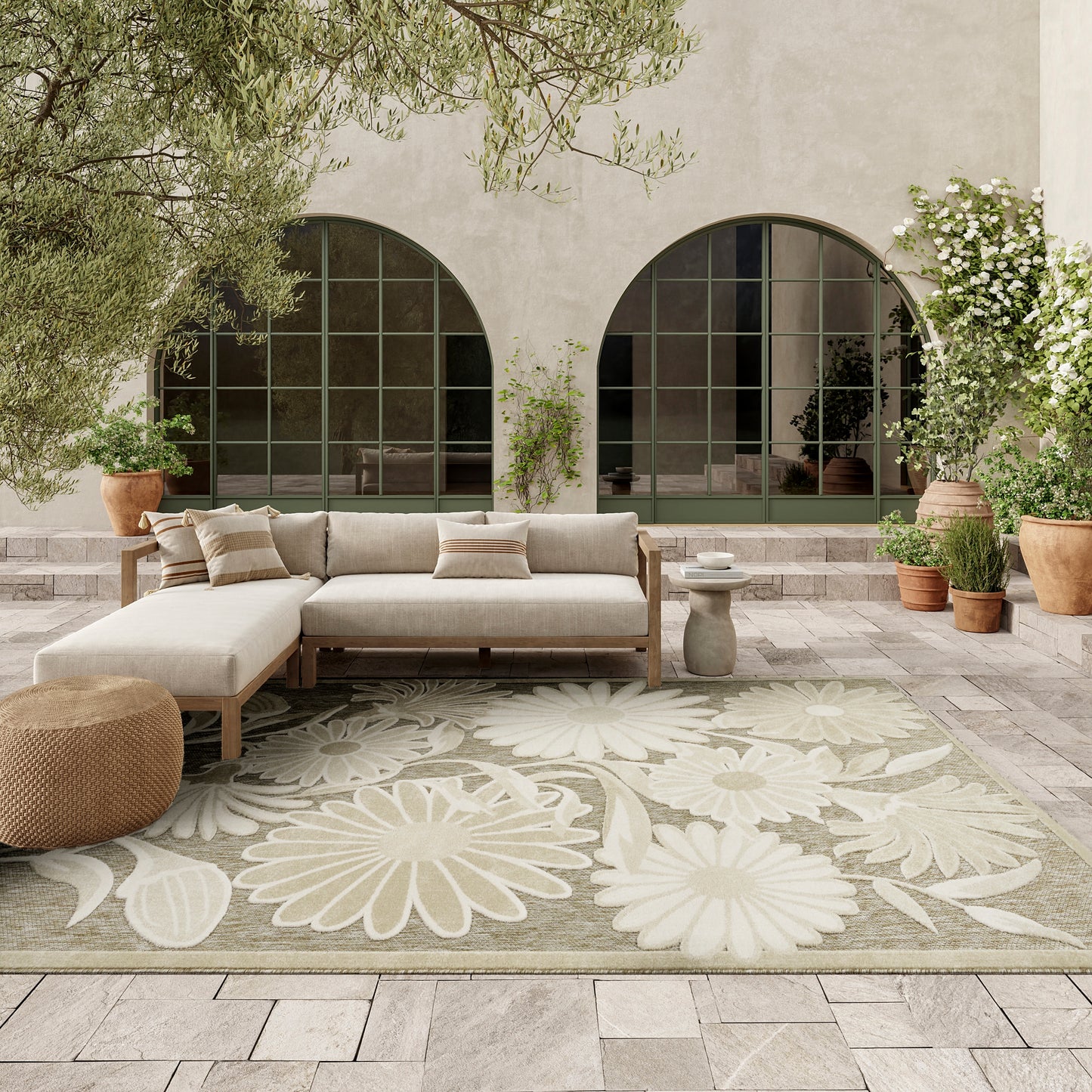 Neutral outdoor lounge with beige sectional sofa, round pouf, large floral rug, and arched green-framed windows.