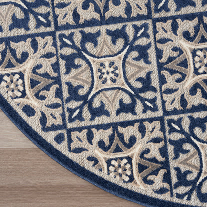 Round beige and navy rug with ornate floral vines and central medallion, plush texture on wooden floor.