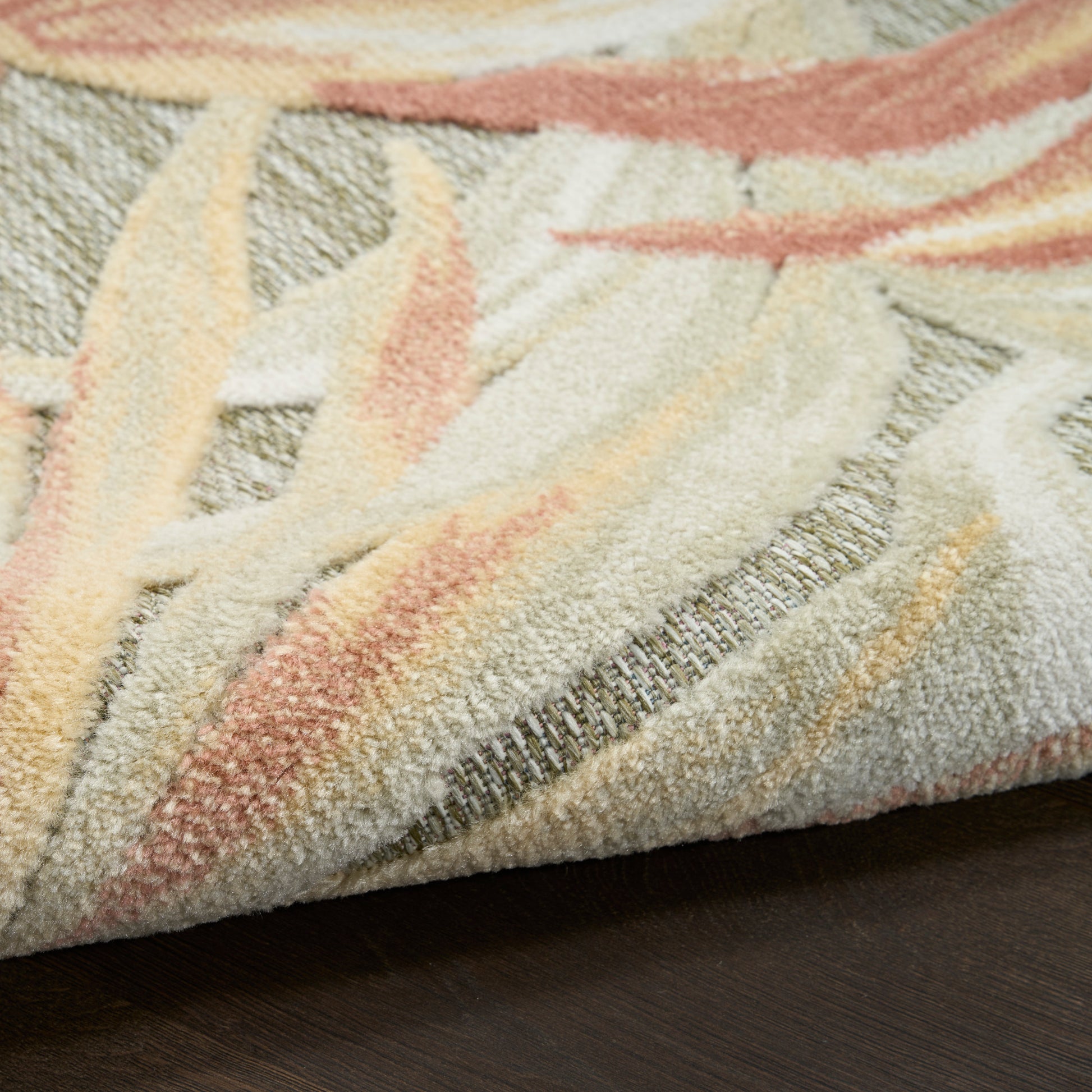 Close-up of a plush pastel rug with cream, peach, pink and sage leaf-like patterns on a dark wood floor.