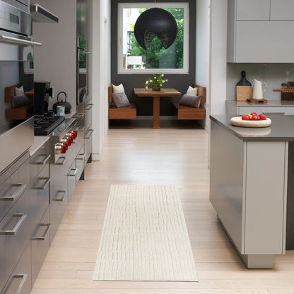 Modern kitchen with white island, light wood floors, beige runner, and dining nook with wooden benches under a black pendant.