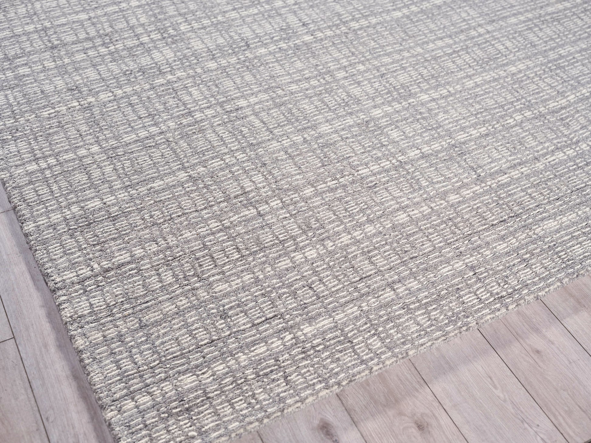 Gray woven area rug with subtle grid texture on light wood flooring.