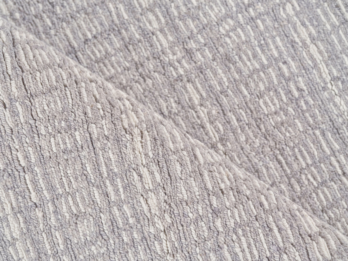 Close-up of a soft gray rug with cream-tinted loop pile and folded edge.