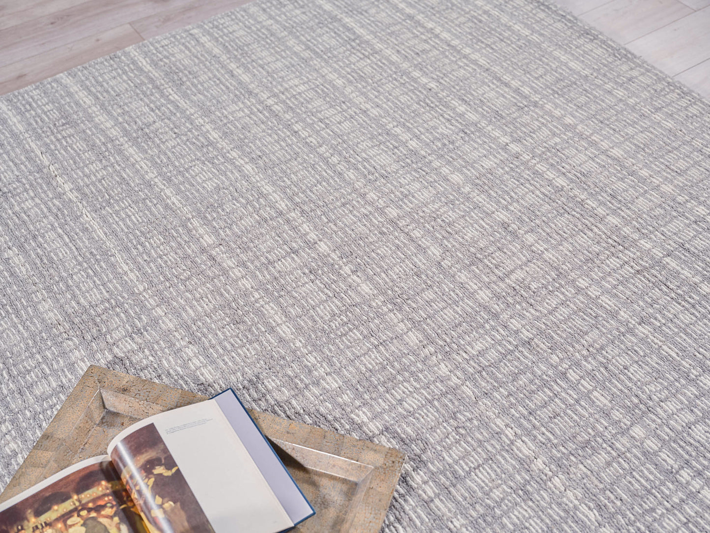 Gray textured area rug with a subtle striped pattern; open book sits on a rustic bronze metal tray.