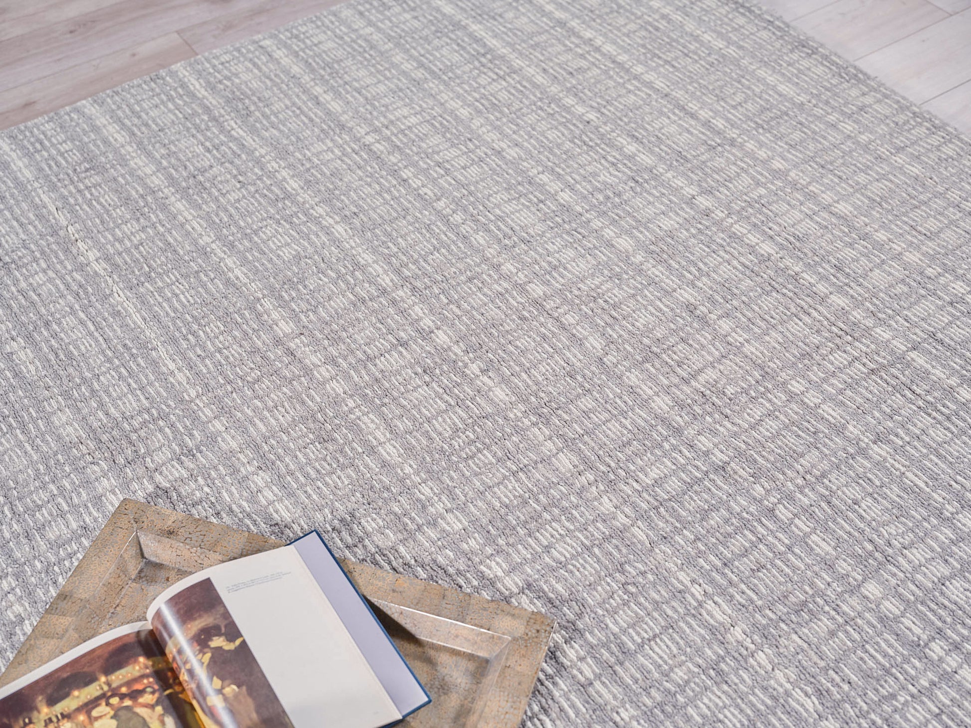 Gray textured area rug with a subtle striped pattern; open book sits on a rustic bronze metal tray.