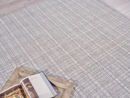 Gray textured area rug with a subtle striped pattern; open book sits on a rustic bronze metal tray.