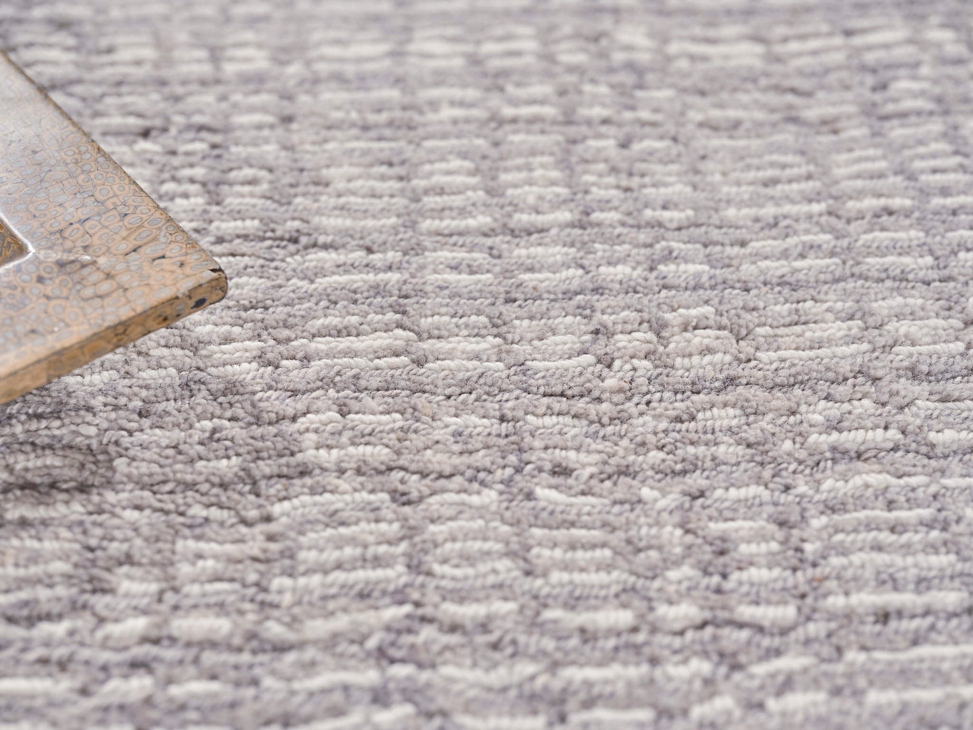 Close-up of a gray textured rug with white speckled pattern; corner of a beige speckled tray resting on it.